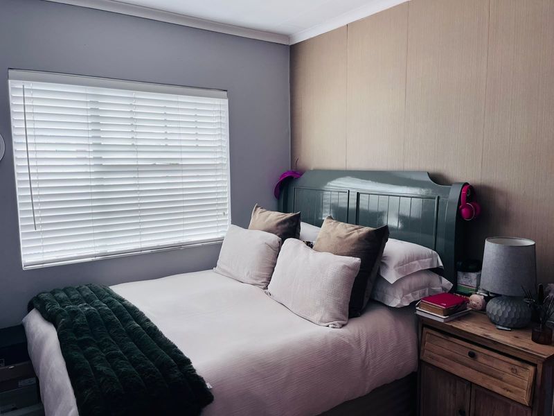 A cozy bedroom featuring wood paneling accent wall and venetian blinds, providing a comfortable and well-maintained sleeping space.