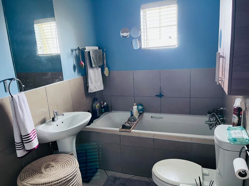A functional bathroom featuring a pedestal sink, a tiled built-in bathtub, and neutral wall tiling with blue accent paint.
