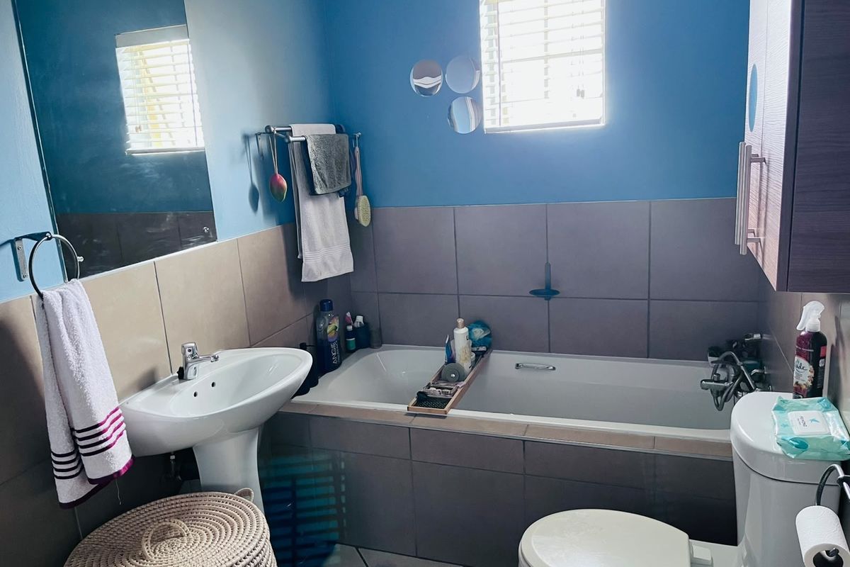 A functional bathroom featuring a pedestal sink, a tiled built-in bathtub, and neutral wall tiling with blue accent paint.