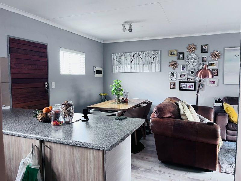 Open plan living and dining area featuring a kitchen island with laminate countertop, light wood-look flooring, and a timber entrance door.