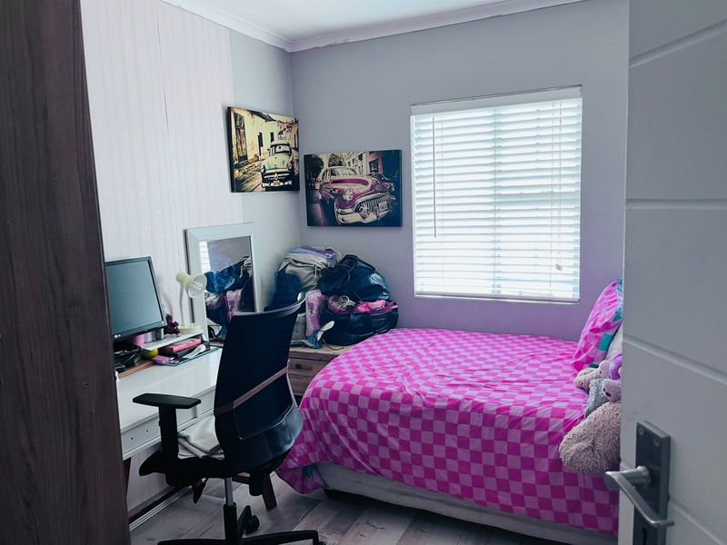 A compact bedroom featuring laminate flooring and a window fitted with venetian blinds, offering a functional space for rest or study.