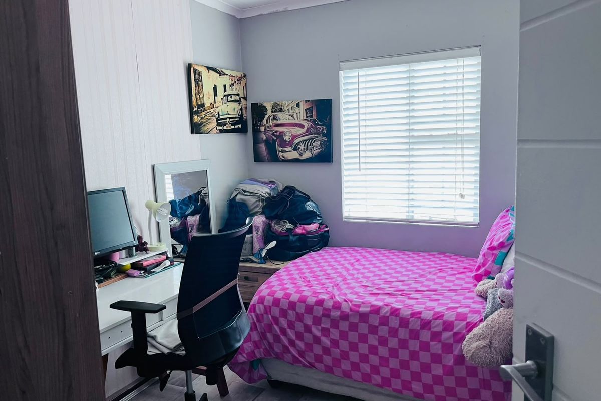 A compact bedroom featuring laminate flooring and a window fitted with venetian blinds, offering a functional space for rest or study.