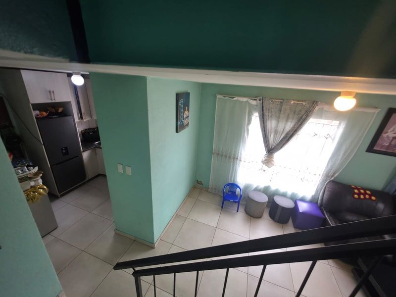 Open plan living area featuring tiled floors and a connected kitchen space, viewed from an elevated staircase position.