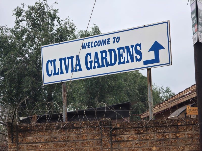 Street-level view of the Clivia Gardens entrance signage, featuring a brick boundary wall topped with security razor wire.