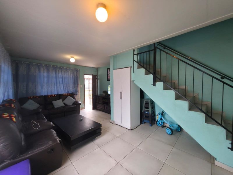 A living room area featuring tiled flooring, a staircase with a metal balustrade, and direct access to the exterior entrance.