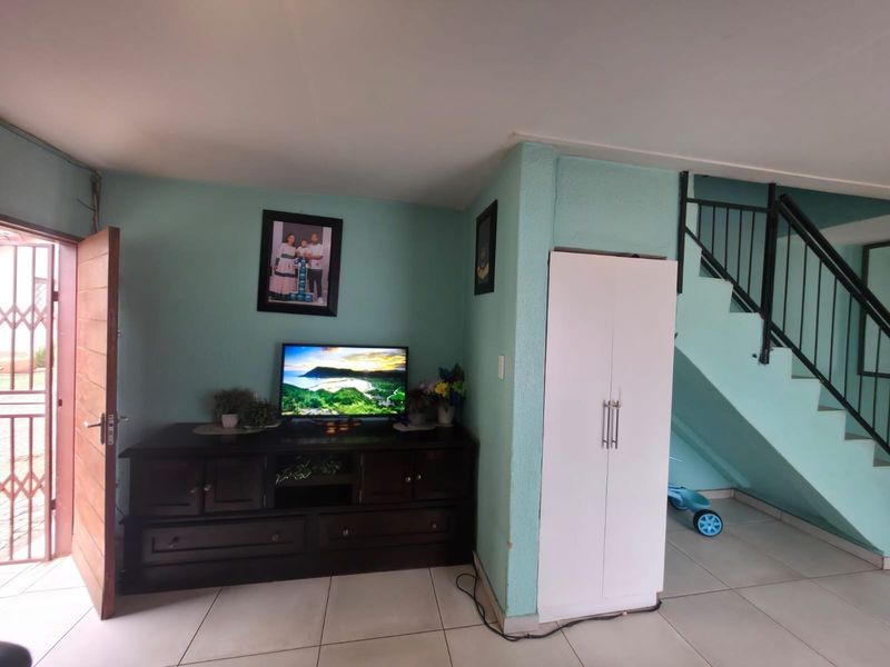 Living area featuring tiled flooring, a staircase with a metal railing, and a built-in storage cupboard.