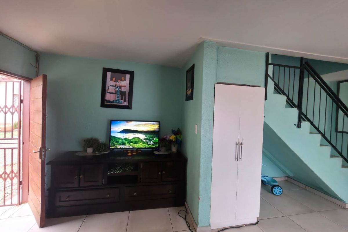 Living area featuring tiled flooring, a staircase with a metal railing, and a built-in storage cupboard.