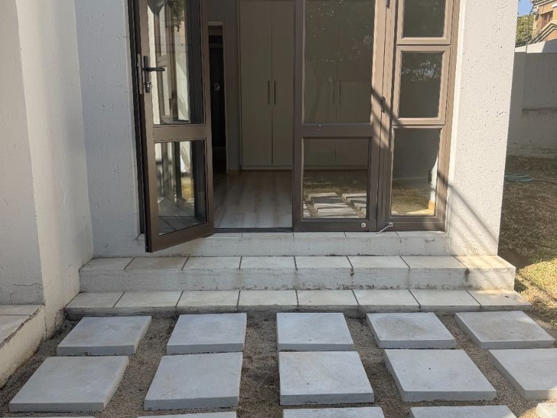 Rear exterior view of a townhouse featuring a paved walkway leading to a glass door entrance with visible interior built-in cupboards.