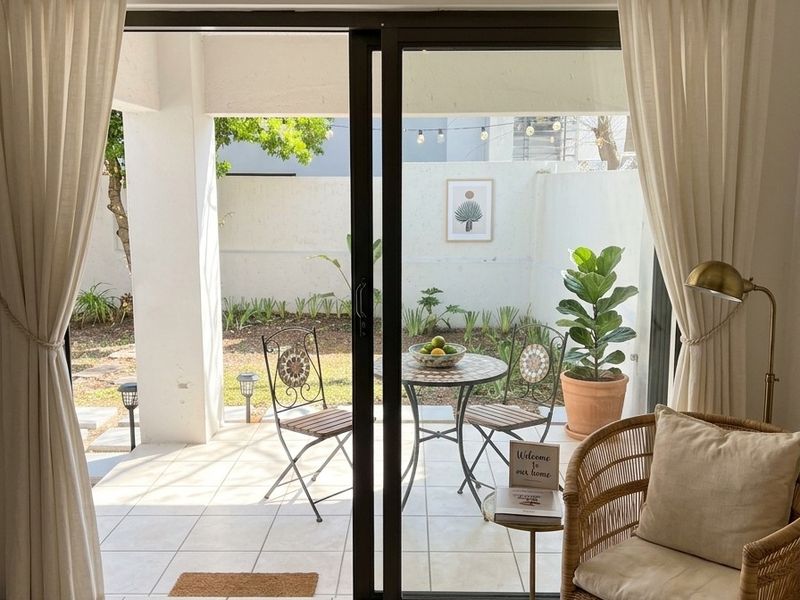 A bright, covered patio area featuring tiled flooring and a sliding glass door, providing a seamless transition to the private garden space.