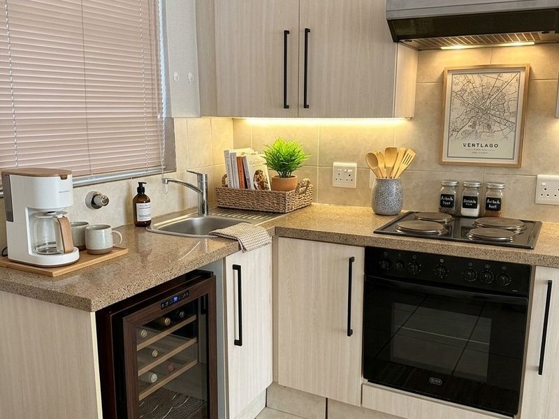 Compact, well-maintained kitchen featuring light wood-finish cabinetry, stone-look countertops, integrated oven, hob, extractor fan, and a convenient under-counter wine cooler.