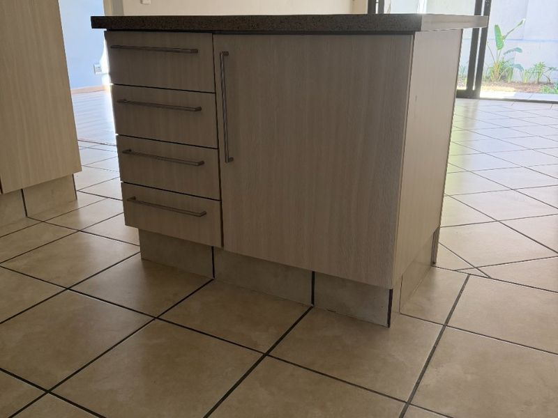 A functional kitchen island with laminate cabinetry and stone countertop, set in an open-plan space with ceramic floor tiles and access to the patio.