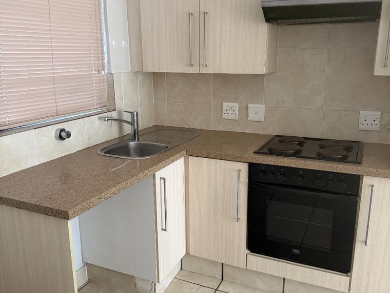 Compact kitchen featuring light wood-finish cabinetry, stone-look countertops, built-in oven and hob, and tiled flooring. Requires minor repairs to cabinetry.