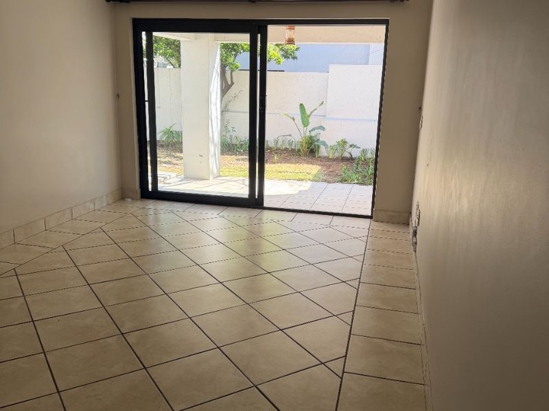 An empty living room featuring neutral ceramic tile flooring and a large sliding glass door providing direct access to the outdoor patio area.