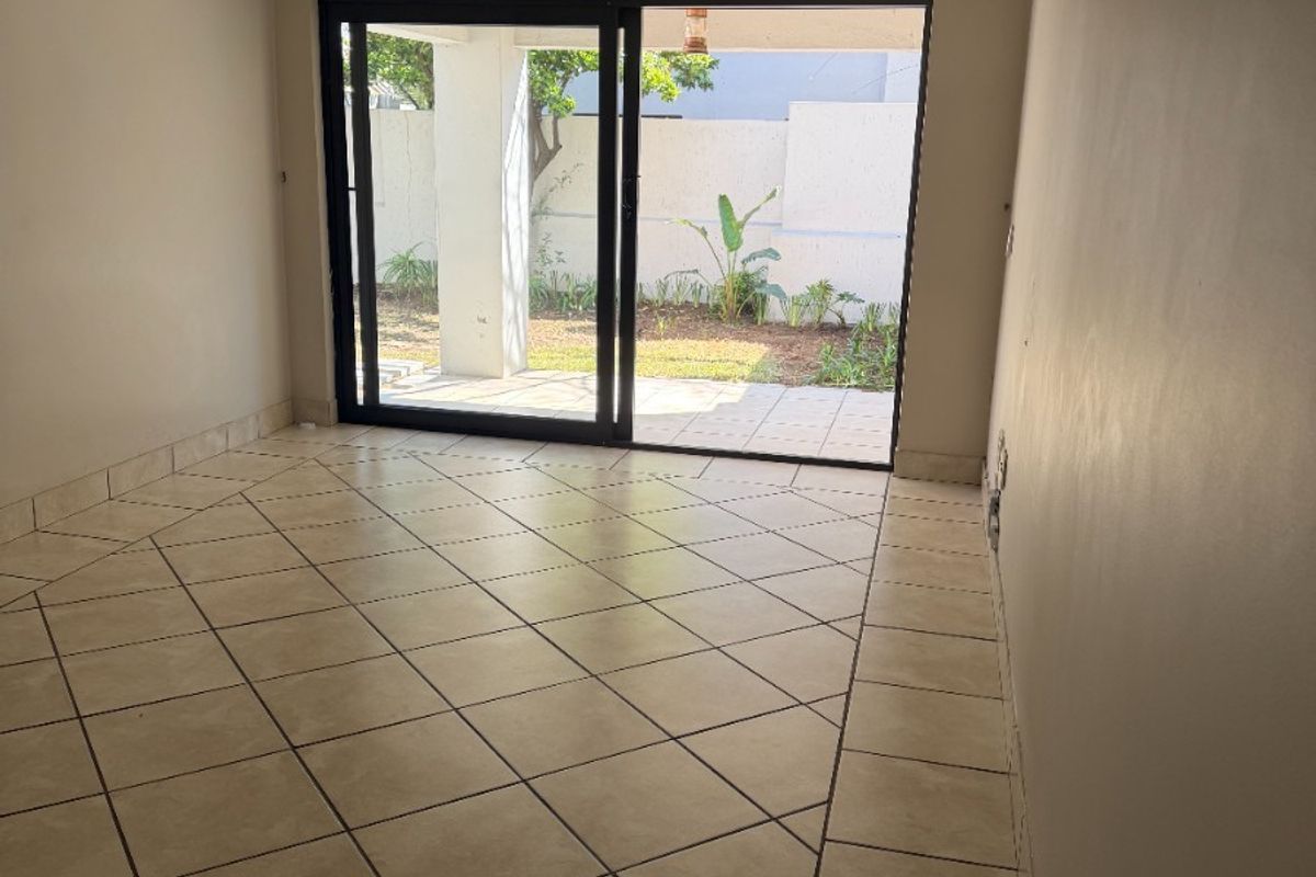 An empty living room featuring neutral ceramic tile flooring and a large sliding glass door providing direct access to the outdoor patio area.