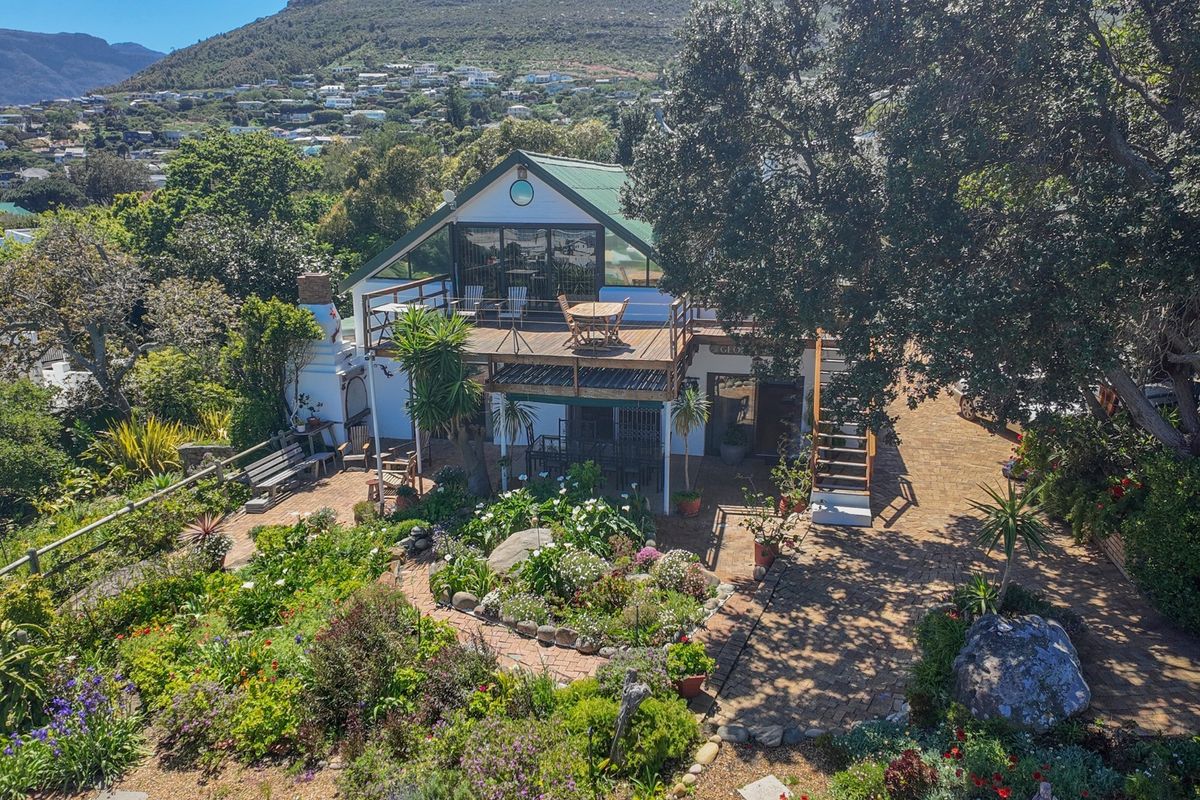 Rear view of the property featuring a raised wooden deck, brick paved patio, and a well-established landscaped garden with mountain views.