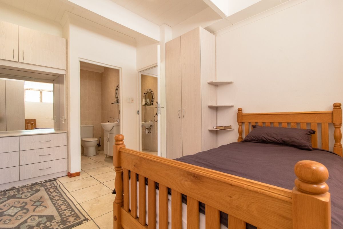 Bedroom featuring built-in cupboards, tiled flooring, and an en-suite bathroom with a vanity and toilet.