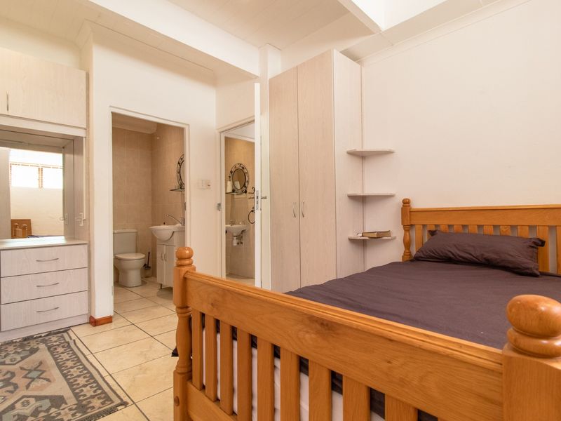 Bedroom featuring built-in cupboards, tiled flooring, and an en-suite bathroom with a vanity and toilet.