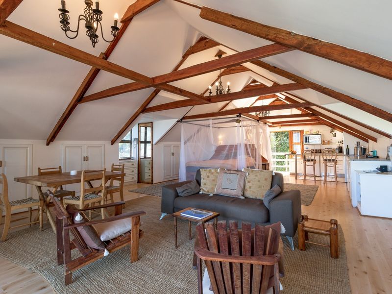 Spacious open-plan living area featuring vaulted ceilings with exposed timber trusses, hardwood flooring, and integrated kitchen cabinetry in a bright, airy loft setting.