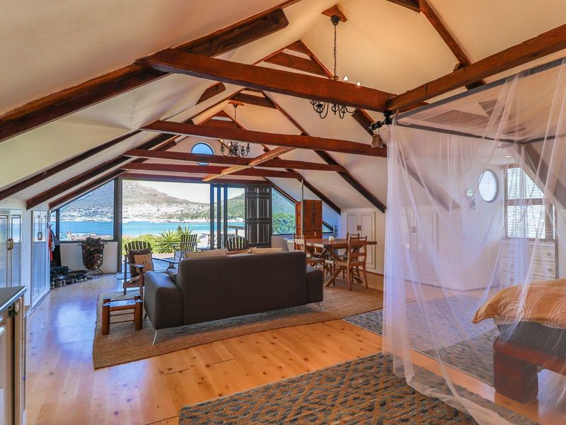 Spacious open-plan living area featuring vaulted ceilings with exposed timber trusses, hardwood floors, and large folding doors opening to a scenic coastal view.