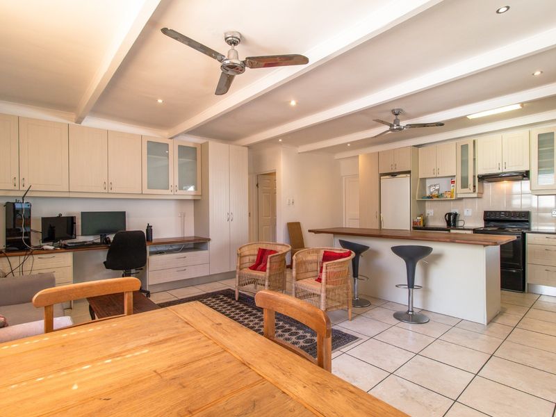 Spacious open-plan living area featuring a functional kitchen with breakfast bar, built-in cabinetry, and a dedicated workspace, all finished with neutral tiled flooring.