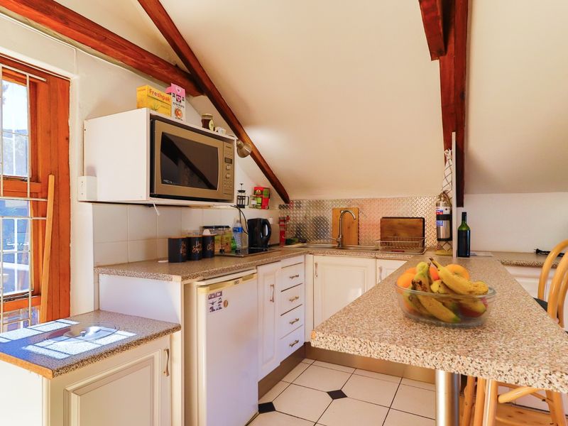 Compact attic-style kitchen featuring exposed timber rafters, granite-look countertops, stainless steel splashback, and tiled flooring with a breakfast bar area.