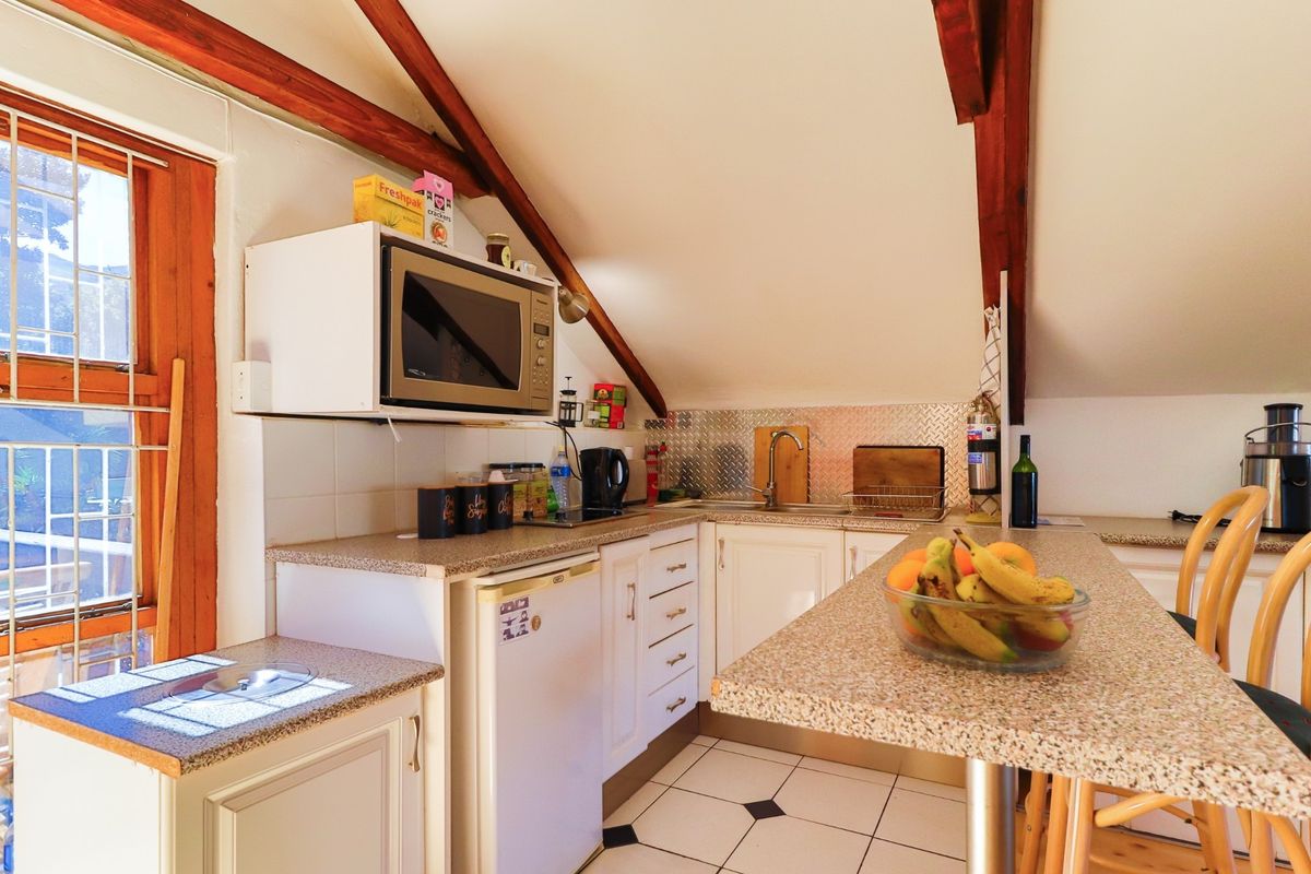 Compact attic-style kitchen featuring exposed timber rafters, granite-look countertops, stainless steel splashback, and tiled flooring with a breakfast bar area.