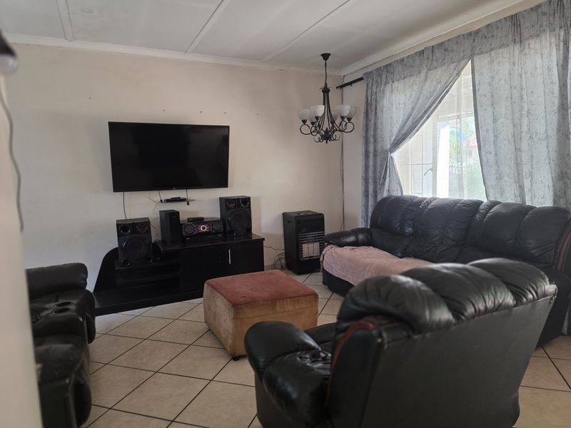 A comfortable living room featuring ceramic floor tiles, a central chandelier, and large windows with curtain rails, offering a functional space for relaxation.