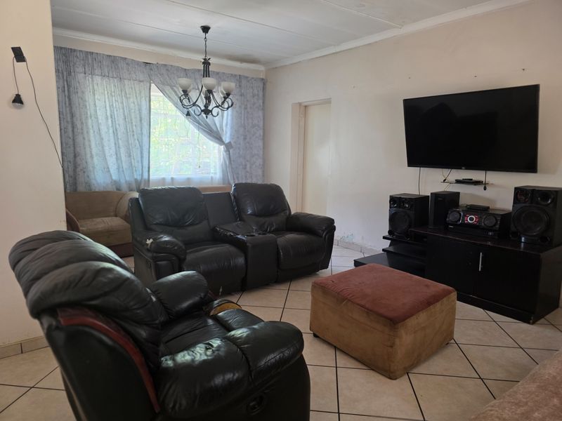 A living room featuring tiled flooring and a central light fixture, requiring cosmetic updates to the walls and general finishes.