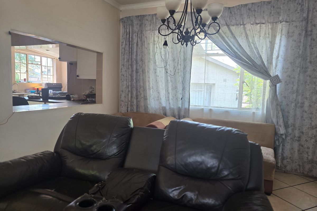 Living room featuring tiled flooring and a serving hatch connecting to the kitchen area, with natural light provided by a large window.