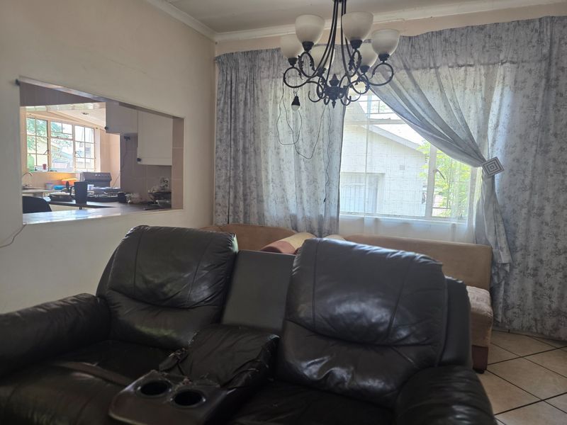 Living room featuring tiled flooring and a serving hatch connecting to the kitchen area, with natural light provided by a large window.