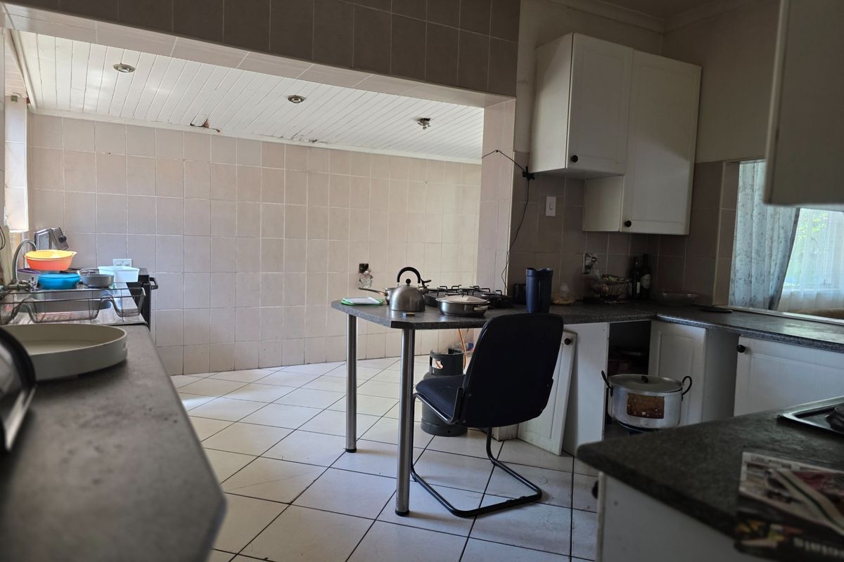 A dated kitchen featuring tiled walls and flooring, built-in cabinetry, and a gas hob, requiring cosmetic updates and repairs to the ceiling and cabinetry.