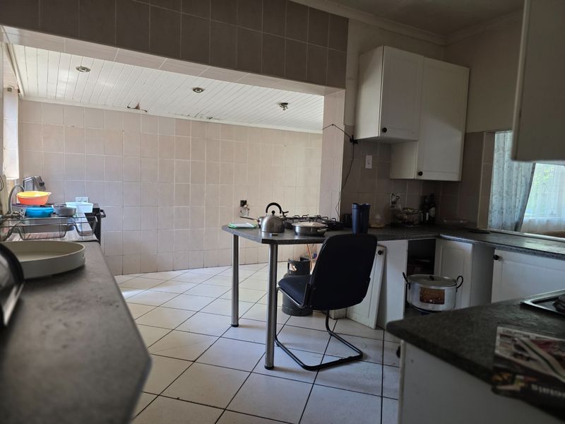 A dated kitchen featuring tiled walls and flooring, built-in cabinetry, and a gas hob, requiring cosmetic updates and repairs to the ceiling and cabinetry.