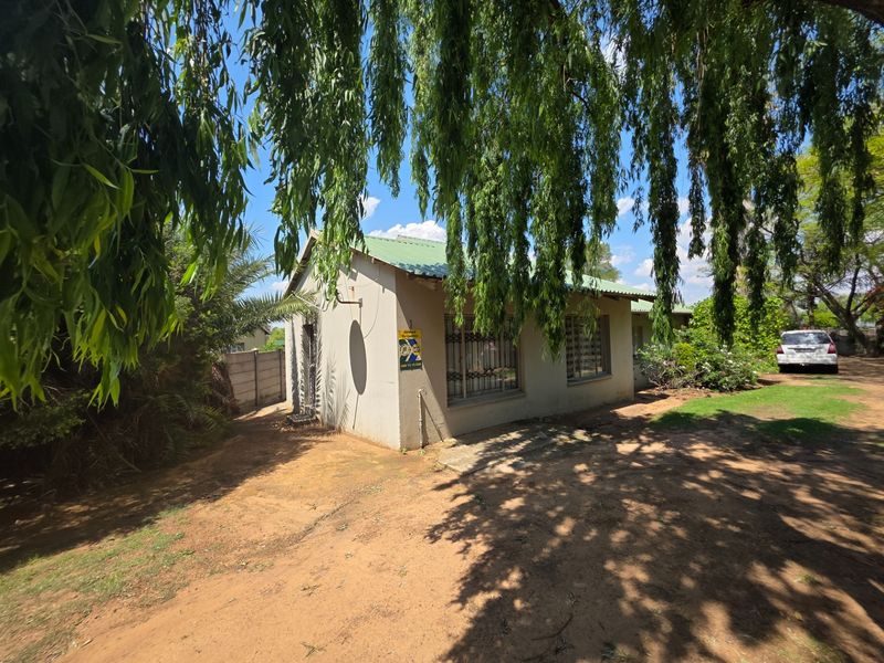 Front exterior view of a single-story house featuring a metal roof, security bars on windows, and a surrounding garden area.