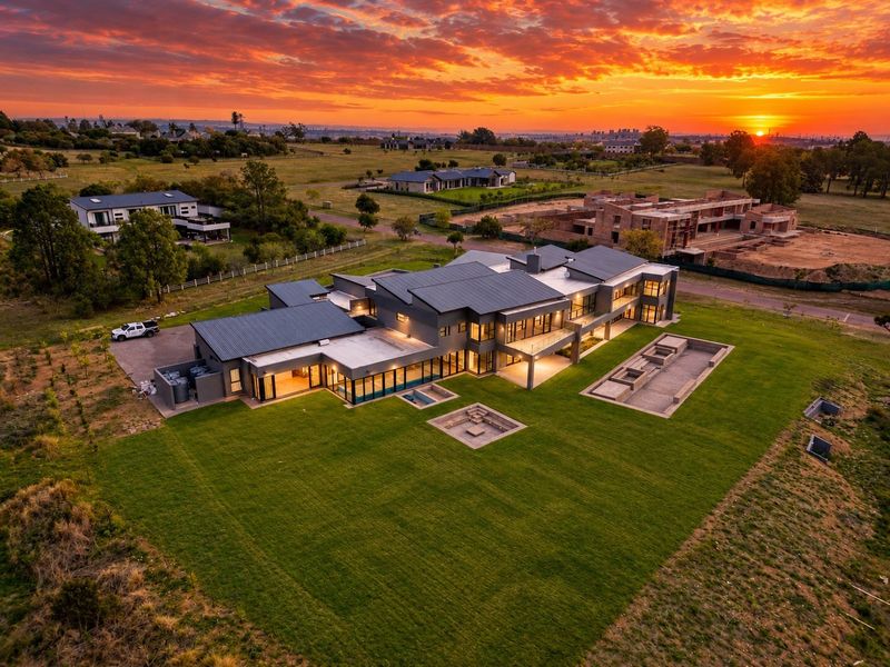 Stunning aerial view of a modern luxury residence at sunset, featuring expansive grounds, a sunken fire pit, and contemporary architectural design.