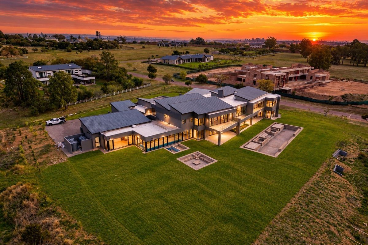 Stunning aerial view of a modern luxury residence at sunset, featuring expansive grounds, a sunken fire pit, and contemporary architectural design.