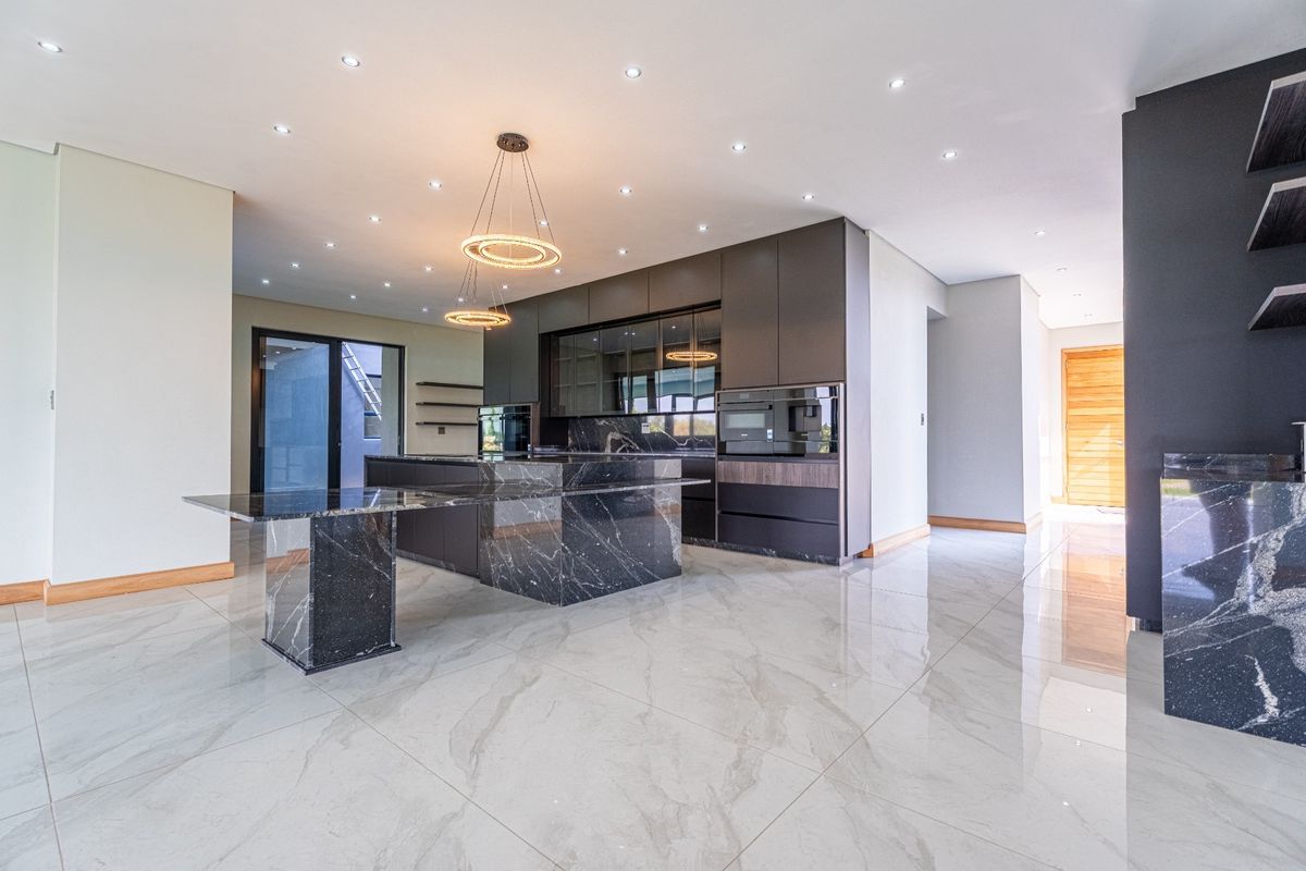 Modern kitchen featuring a large marble island, dark cabinetry, built-in appliances, and polished porcelain floor tiles in an open-plan layout.