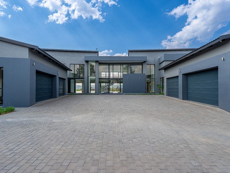 Modern architectural front elevation featuring a spacious paved driveway, multiple garage bays, and a striking glass-fronted entrance.