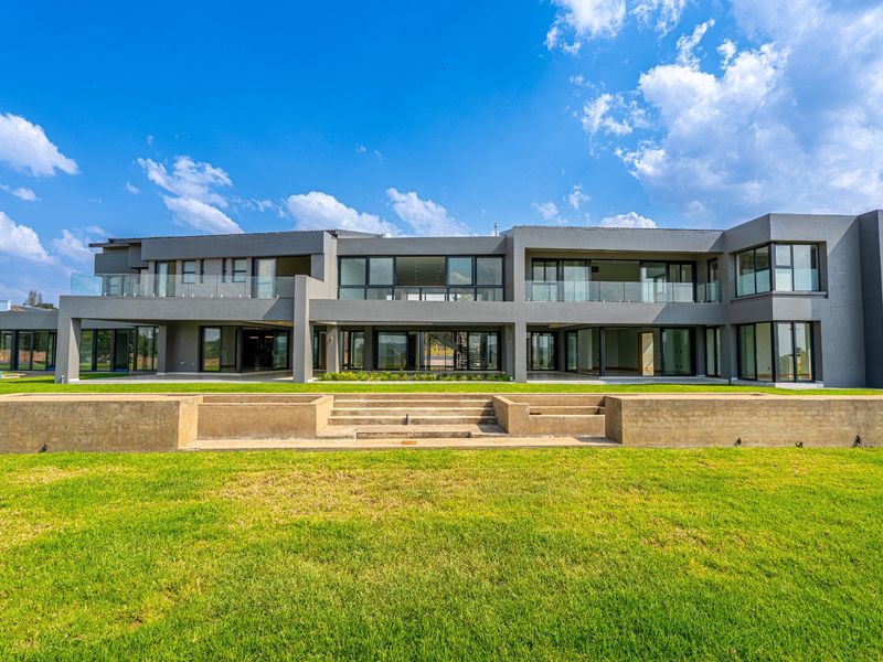 A modern double-story rear elevation featuring extensive glass sliding doors, glass balustrades, and a tiered concrete retaining wall overlooking a spacious lawn.