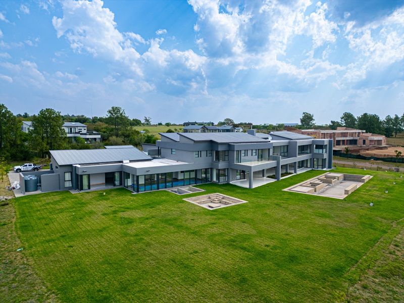 Aerial view of a modern, expansive luxury residence featuring a large lawn, swimming pool, covered patio, and contemporary architectural design.