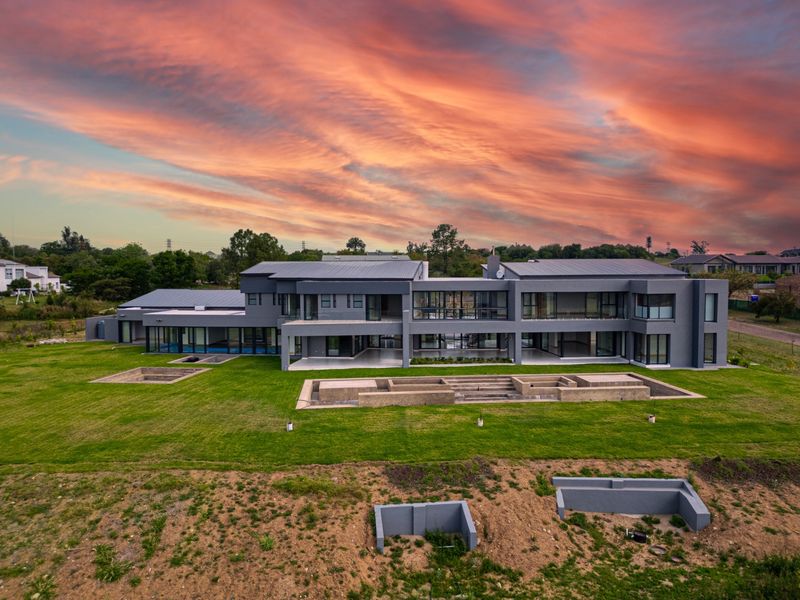 Aerial view of a modern, large-scale luxury residence featuring extensive glass facades, metal roofing, and expansive grounds with unfinished landscaping elements.