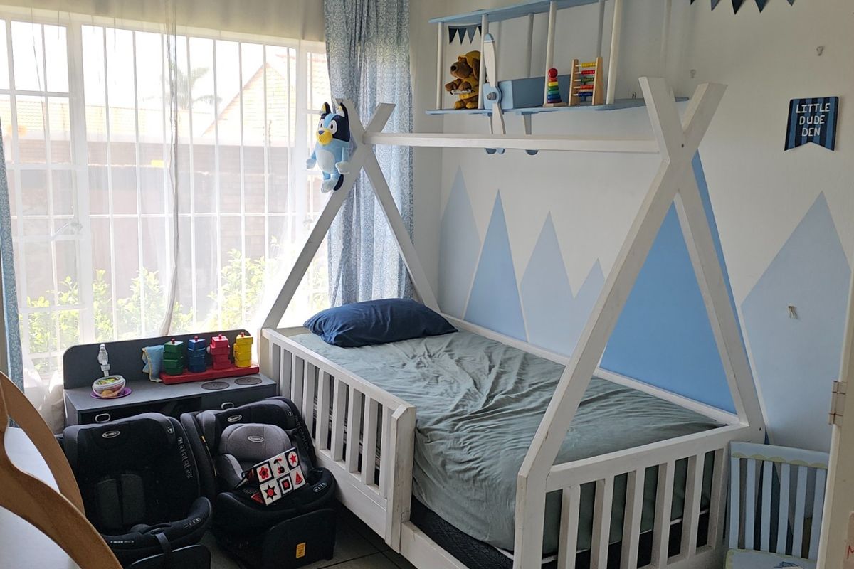 A bright bedroom featuring tiled flooring and large windows fitted with security bars, currently utilized as a child's room.