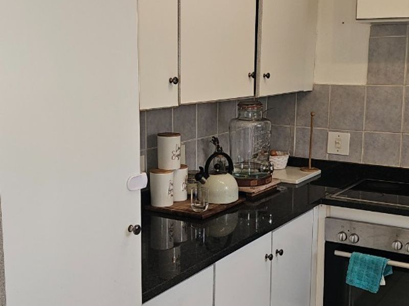 A functional kitchen featuring white cabinetry, dark granite countertops, tiled backsplash, and integrated oven and hob.