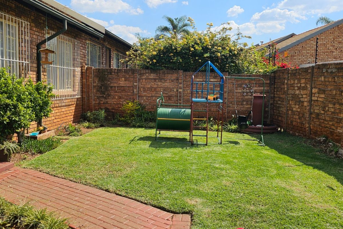 A private rear garden featuring a well-maintained lawn, brick paving, and secure perimeter walling with electric fencing.