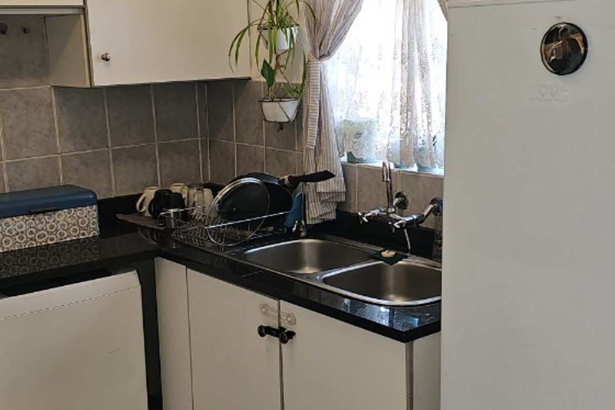 A compact kitchen featuring white cabinetry, dark laminate countertops, a double bowl sink, and tiled flooring, offering a functional layout with potential for modernization.