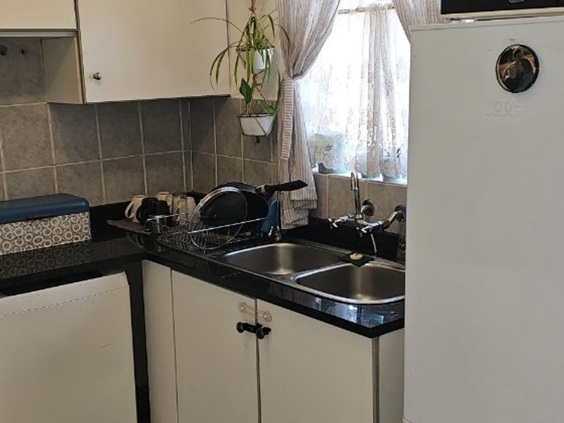 A compact kitchen featuring white cabinetry, dark laminate countertops, a double bowl sink, and tiled flooring, offering a functional layout with potential for modernization.