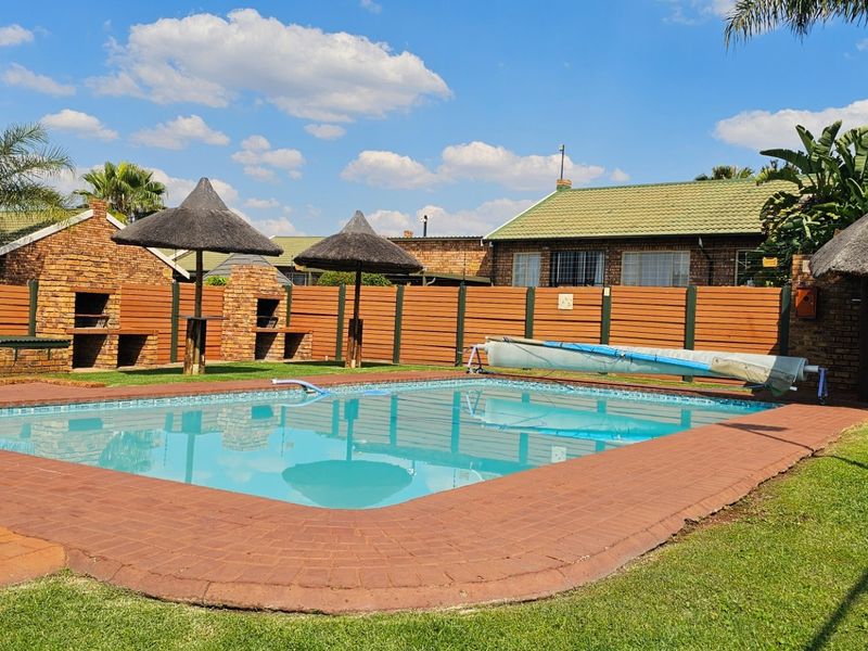 Outdoor pool area featuring a swimming pool with a cover, brick paving, built-in braai facilities, and a thatched lapa for entertainment.
