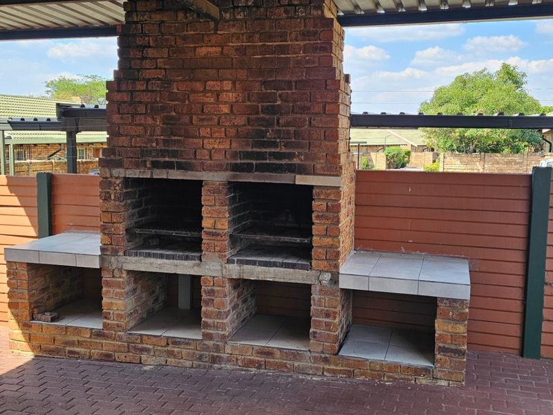 Covered outdoor patio featuring a large built-in brick braai with tiled prep surfaces and paved flooring, ideal for outdoor entertaining.