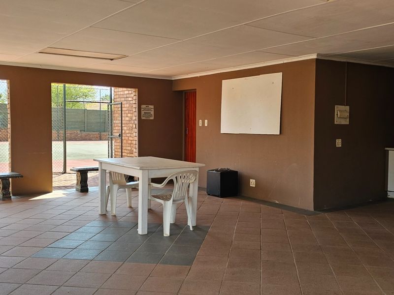 A covered outdoor patio area featuring tiled flooring, built-in cabinetry, and direct access to the adjacent tennis court.