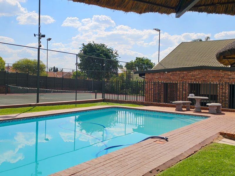 Outdoor entertainment area featuring a swimming pool, brick-paved surround, thatch lapa, and access to a private tennis court.