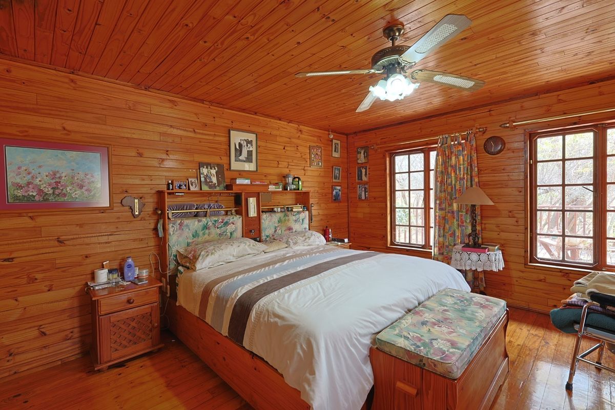 A cozy bedroom featuring warm timber wall cladding, matching wood ceiling and flooring, and a functional ceiling fan with integrated lighting.